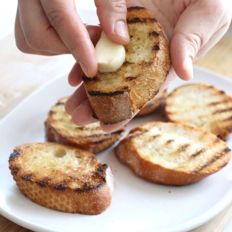 마늘 끝을 살짝 잘라낸 뒤 구운 바게트에 잘라낸 마늘 단면을 문질러 마늘 향이 배어 나도록 해주세요.