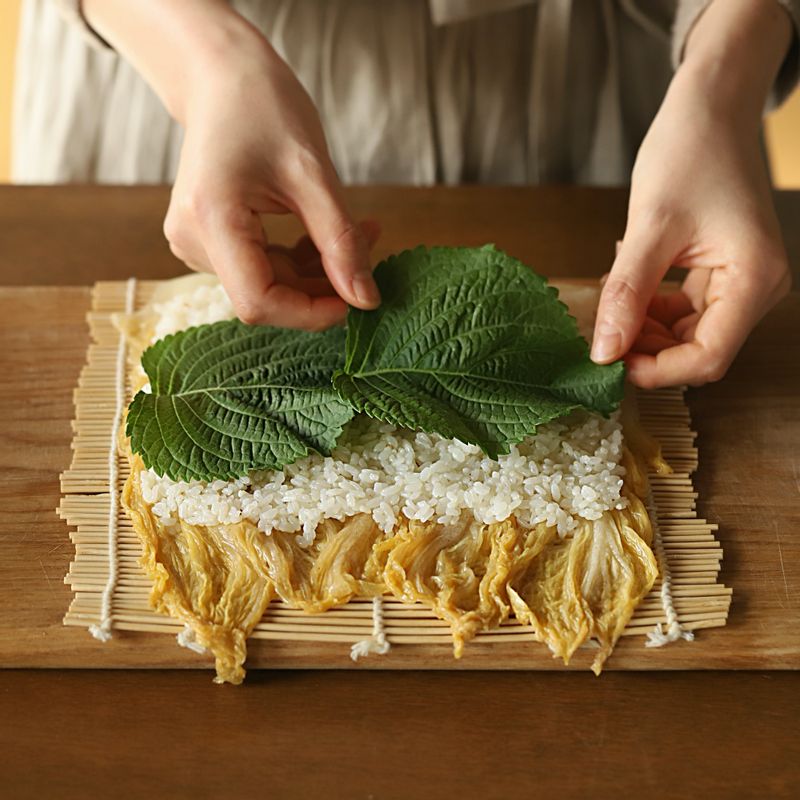 김발에 묵은지를 넓게 펼쳐주세요. 밥을 고르고 얇게 펴고 깻잎을 깔아주세요. 참치장을 적당량 올린 후 묵은지를 말아주세요.
