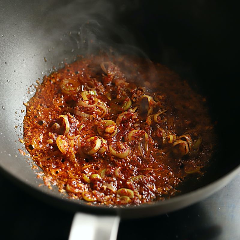 달군 팬에 식용유를 넉넉히 두르고 대파와 마늘을 넣어 볶다가 고춧가루를 넣고 중약불에서 볶아주세요.
