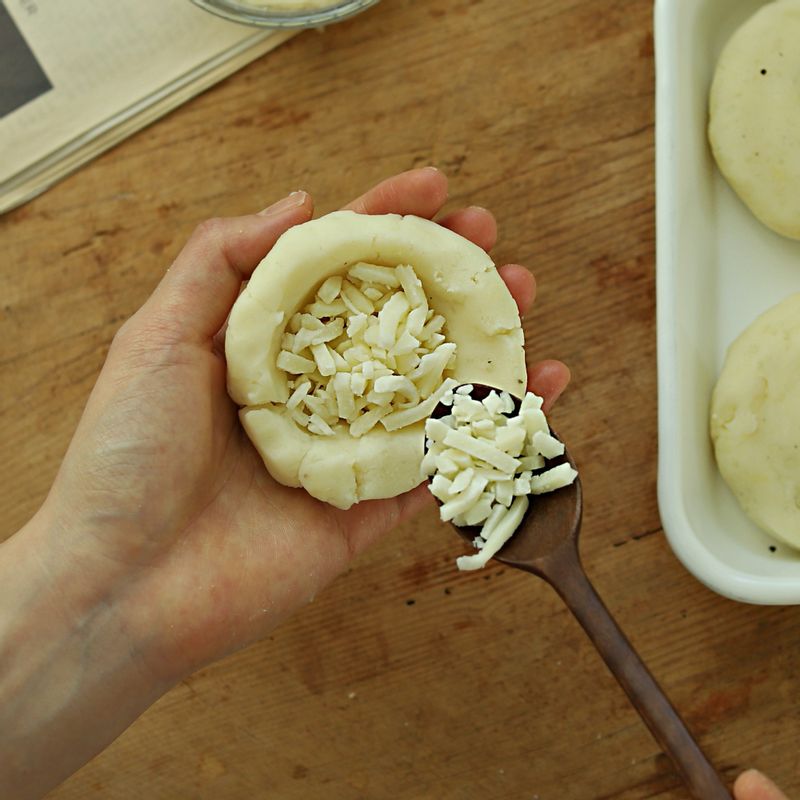 감자 반죽을 80g 정도의 적당한 크기로 떼어내 가운데에 모차렐라 치즈를 넣어 동글납작하게 만들어주세요.
(구울 때 치즈가 새어 나오지 않도록 이음새 부분을 꼼꼼하게 눌러주세요)
(tip. 속 재료는 토마토소스, 흑설탕 등으로 다양하게 응용해도 좋아요)