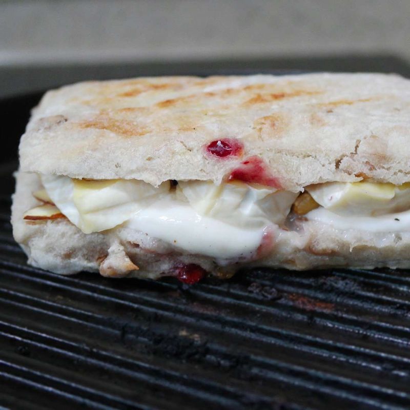 그릴팬을 달군 후 빵을 올리고 무거운 냄비나 뚜껑으로 눌러주세요. 치즈가 녹을 때까지 앞뒤로 구워주세요. 꿀 1/2큰술을 뿌리고 남은 호두와 아몬드 슬라이스를 뿌려냅니다.