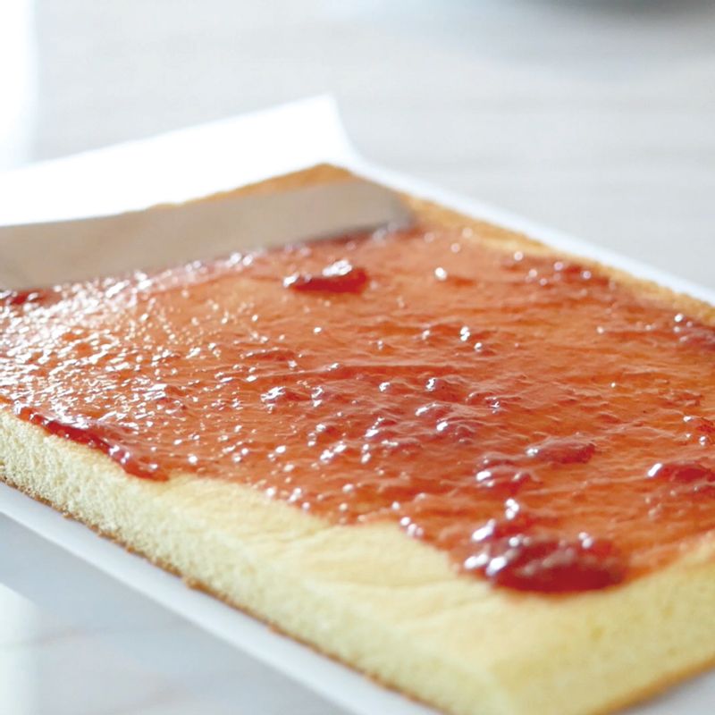 16. 반죽 표면에 딸기잼을 발라주세요.
(Tip! 잼이 없다면 꿀로 대체해도 무방합니다.)
17. 칼집을 낸 반죽 방향에서 대각선으로 비스듬하게 자른 반죽을 향해 유산지 끝부분을 붙잡 고 천천히 말아줍니다.
18. 종이로 반죽을 감싼 채 타이트하게 당겨서 잘 말아주고 테이프를 붙여 고정한 뒤 냉장실 에 1시간 정도 보관합니다.
19. 냉장고에서 꺼낸 순서18의 종이를 제거하고 먹을 만큼 자릅니다.
레시피 영상 : https://youtu.be/-6oKEiI6_N0