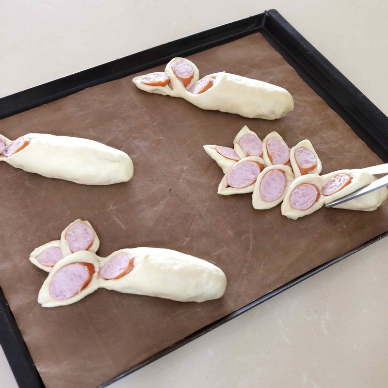 10. 반죽의 매끈한 면이 위로 가도록 팬에 놓고 가위를 45도 각도로 세워 끝부분을 조금 남기며 7번 잘라주세요. 잘린 반죽을 지그재그 형태로 놓아주세요.
11. 반죽의 표면이 마르지 않도록 랩으로 덮고 부피가 2배로 늘어날 때까지 2차 발효해주세요.