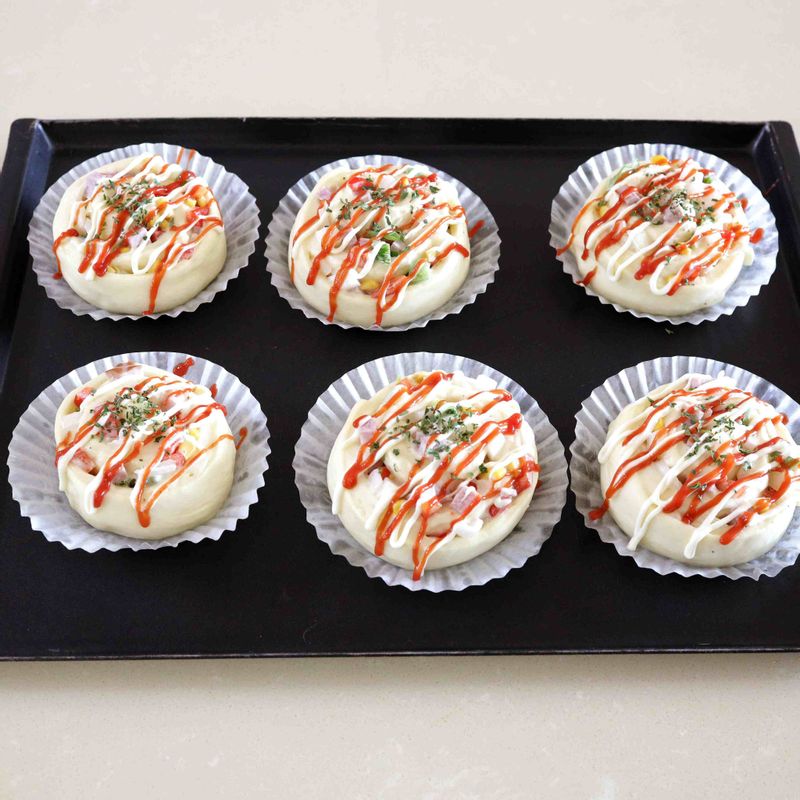 14. 미리 만들어둔 달걀물을 붓에 묻혀 반죽의 매끈한 면만 발라 준 후 마요네즈와 케첩, 파슬리를 올려 장식합니다. 170~180°C로 예열된 오븐에 반죽을 넣고 12~15분 정도 구워주세요.
15. 잘 익은 반죽을 오븐에서 꺼내자마자 팬을 20~30cm 높이로 들고 큰 소리가 날 정도로 내리쳐 쇼크를 주고 빵을 식힘망에 올려 식혀주세요.