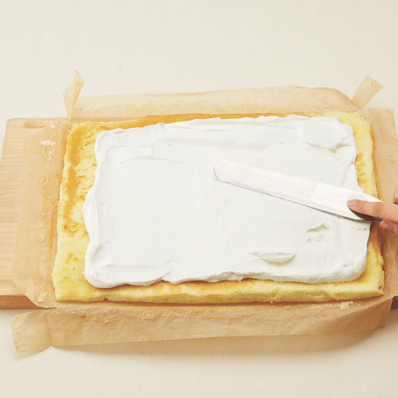 12. 떼어낸 유산지 위에 롤 케이크를 올리고 크림을 올립니다. 스패튤라를 좌우로 움직여 크림을 살짝 누른다는 느낌으로 펴 바른 후 딸기와 키위를 골고루 올려주세요.
(tip. 롤 케이크를 말 때 생크림이 뒤로 밀리니 윗쪽에 2cm 정도의 공간을 남겨 두세요.)
13. 롤 케이크의 한쪽 끝 부분을 사진처럼 손가락으로 눌러 1cm 정도 높이로 접어 올려주세요.
(tip. 스패튤라로 끝 부분의 1.5cm 정도 위치를 가볍게 눌러 자국을 내어 말면 더 쉽게 말 수 있어요.)
14. 김밥을 말듯이 돌돌 말아준 다음 유산지로 감싸 냉장실에서 30분 이상 굳힙니다.
(tip. 롤 케이크를 말 때는 재빨리 말아야 찢어지거나 갈라짐이 생기지 않아요.)