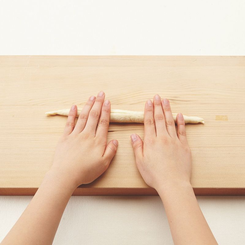 10. 가운데는 볼록하고 양쪽 끝으로 갈수록 얇아 지도록 손바닥으로 밀어 가며 50cm 길이로 늘려주세요.
(tip. 손바닥에 물을 약간씩 묻혀 밀면 더 잘 늘어나요.)
11.	반죽의 양쪽 끝을 잡고 두 번 꼬아주세요. 끝 부분에 물을 바르고 사진처럼 볼록한 가운데 부분에 간격을 두고 붙입니다.
12.	유산지를 깐 오븐 팬에 반죽을 올려주세요. 뜨거운 물과 베이킹소다를 섞은 후 숟가락으로 골고루 끼얹습니다. 팬을 살짝 기울여 고인 물을 따라내어주세요.
(tip. 뜨거운 물을 끼얹어 주면 반죽이 좀 더 쫄깃해 져요. 이 과정은 생략해도 좋아요.)
13.	반죽 윗면에 붓으로 물을 바르고 토핑용 설탕과 시나몬가루를 골고루 뿌립니다. 아몬드 슬라이스를 올린 후 살짝 눌러 붙여주세요.