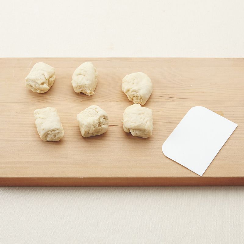 7. 덧밀가루를 뿌린 도마나 작업대 위에 순서6의 반죽을 올립니다. 손바닥으로 눌러 가스를 뺀 후 스크래퍼로 약 50g씩 6등분해주세요.
(tip. 반죽하는 방법에 따라 반죽 양이 조금씩 달라질 수 있어요. 총 무게를 저울로 잰 후 6등분하세요.)
8. 손으로 둥글리기 한 후 젖은 면보(또는 비닐)를 덮어 실온(27℃)에서 15~20분간 중간 발효시켜주세요.
9. 도마나 작업대 위에 반죽의 밑부분이 위로 가도록 놓고 12cm 길이의 긴 타원형으로 밀대로 밀어 핍니다. 사진처럼 돌돌 말아 이음새 부분을 꼬집어 붙여주세요.
(tip. 반죽 속에 공기가 들어가지 않도록 주의하며 말아요.)