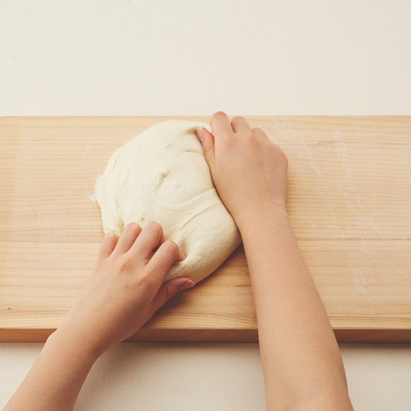 4. 반죽이 한 덩어리가 되면 도마 또는 작업대 위에 올립니다. 반죽을 양손으로 잡고 바닥에 짓이기듯이 손바닥으로 눌러 펴주세요. 다시 반으로 접어 눌러 펴며 10~15분간 반죽합니다.
5. 반죽을 둥글리기 한 후 볼에 넣어주세요. 큰 볼에 뜨거운 물을 넣고 그 위에 반죽을 넣은 볼을 올린 후 랩을 씌웁니다. 따뜻한 곳(28~30℃)에서 40~60분간 반죽이 2배의 크기가 될 때까지 1차 발효시켜주세요.
6. 덧밀가루를 뿌린 도마나 작업대 위에 반죽을 올립니다. 손바닥으로 눌러 가스를 뺀 후 스크래퍼로 약 185g씩 6등분해주세요. 
(tip. 반죽하는 방법에 따라 반죽 양이 조금씩 달라질 수 있어요. 반죽의 총 무게를 저울로 잰 후 6등분하세요.)