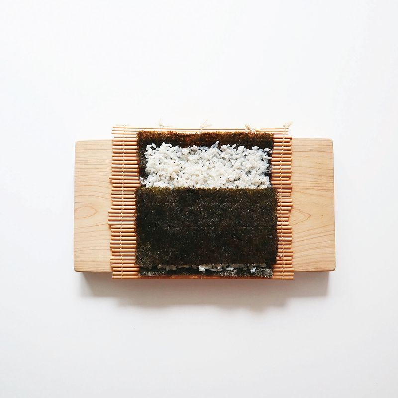 김발에 거친 면이 위로 올라오도록 김밥 김 1장을 펼치고, 양념한 밥을 얇게 펴 올린 뒤 김밥 김 1/2장을 덮어주세요.