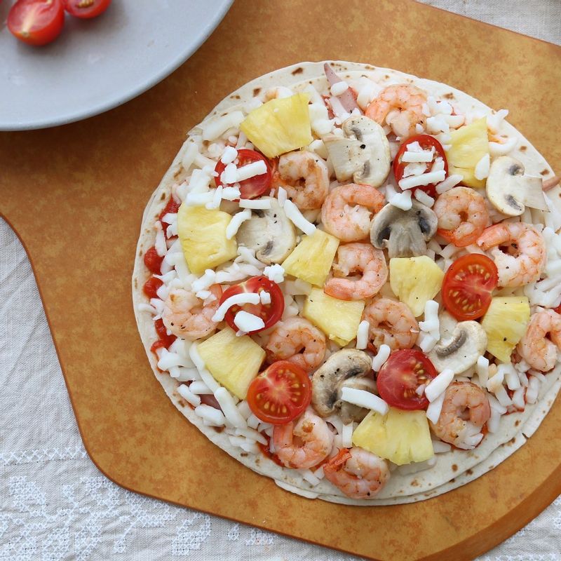 방울토마토, 양송이버섯, 파인애플, 칵테일새우를 올린다. 팬 뚜껑을 덮고 치즈가 녹을 때까지 약한 불로 12~15분간 구워주세요.
200도로 예열한 오븐에 넣어 10분간 구우면 좀 더 바삭한 피자를 만들 수 있어요.