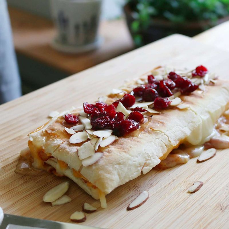 달군 팬에 올리브오일을 두르고 빵을 올려 4~5분간 노릇하게 구워주세요. 빵 위에 꿀을 뿌린 후 아몬드슬라이스와 건크랜베리를 얹고 3등분합니다.