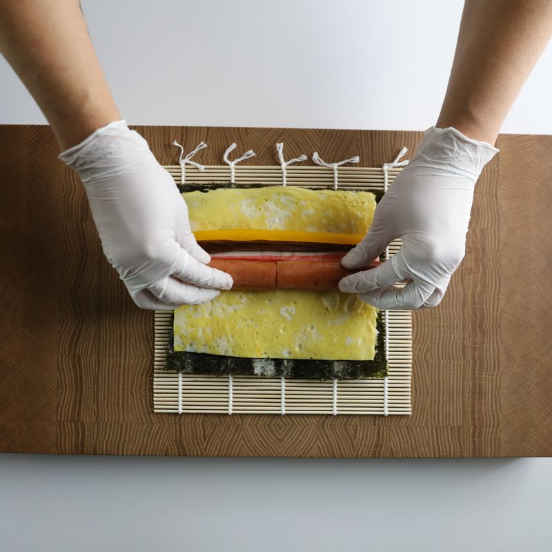 얇게 편 밥 위에 달걀지단을 올리고 조림우엉, 단무지, 맛살, 프랑크소시지를 올린 뒤 머스터드소스를 뿌려주세요.