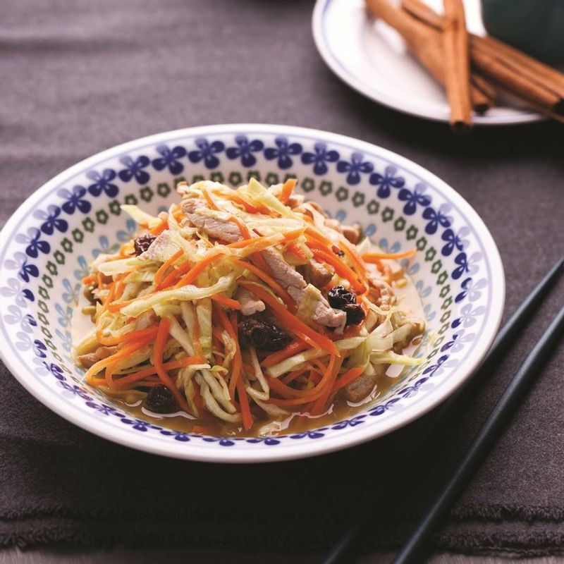 채 썬 양배추와 당근, 볶은 돼지고기를 그릇에 담고 드레싱과 다진 아몬드를 뿌려 맛있게 즐기세요.