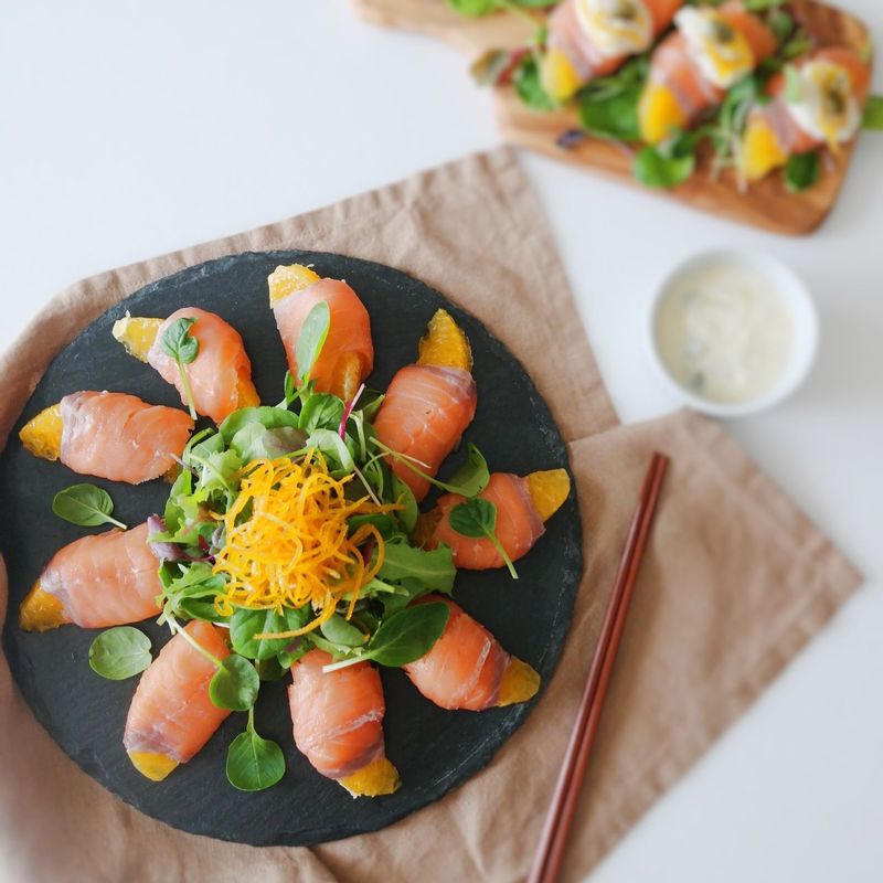 칼로 오렌지의 속껍질을 벗겨내고 과육만 훈제연어로 돌돌 말아주세요. 그릇에 어린잎채소, 오렌지제스트, 케이퍼와 함께 담아낸 후 먹기 전에 드레싱을 뿌려주세요.