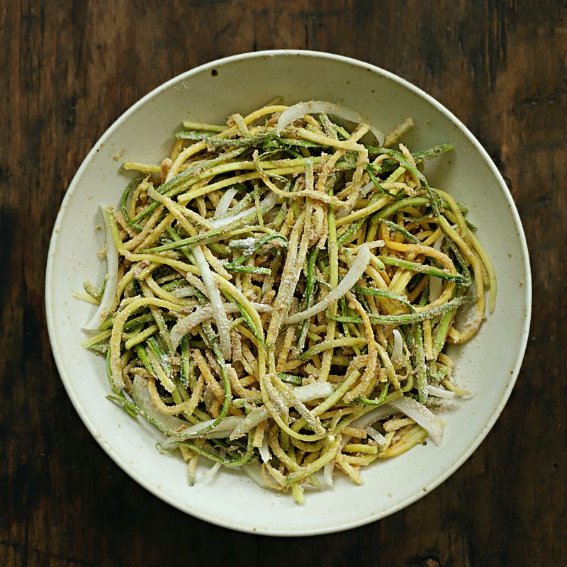 애호박에 소금을 넣고 가볍게 버무린 후, 양파와 통밀가루를 넣고 섞어주세요.