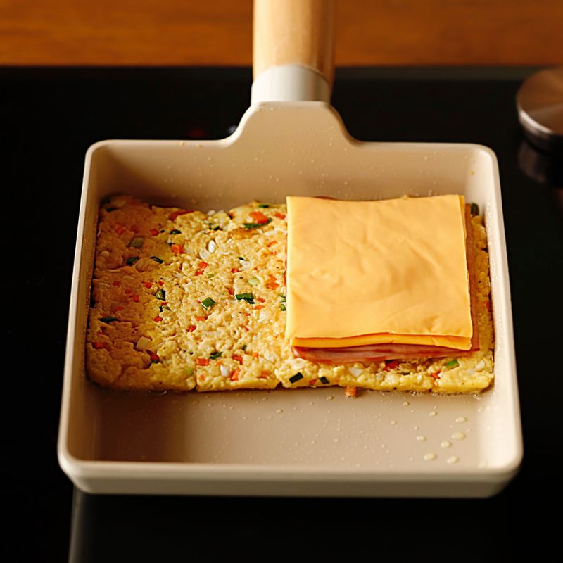 달군 팬에 기름을 약간 두른 후 반죽을 잘 펼쳐 뒤집개로 모양을 잡고 치즈와 햄을 올려주세요.