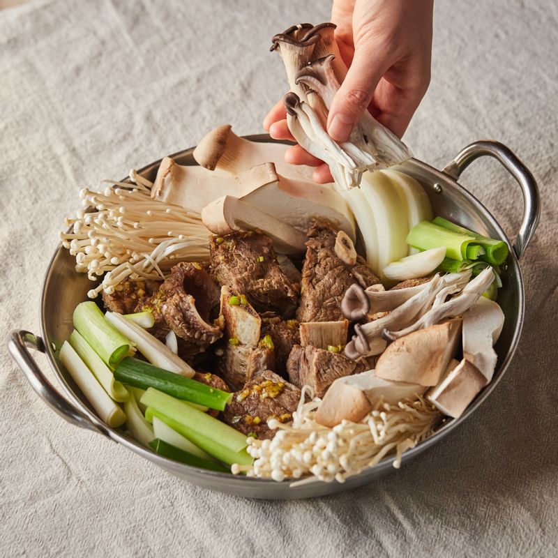 전골냄비에 소갈비를 담고 양념장과 버섯과 대파, 콩나물과 미나리, 불린 납작 당면 순으로 담은 후 육수 5컵을 부어주세요.