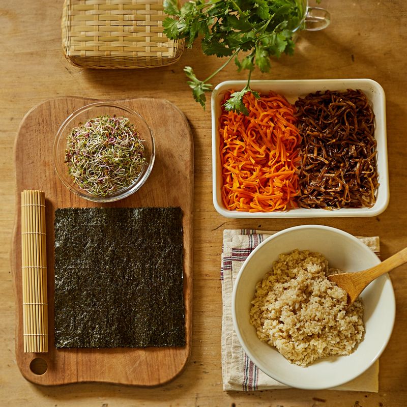 김발에 김을 올리고 현미밥을 고르게 편 후 우엉, 당근, 새싹 채소를 올려 김밥을 말아주세요.