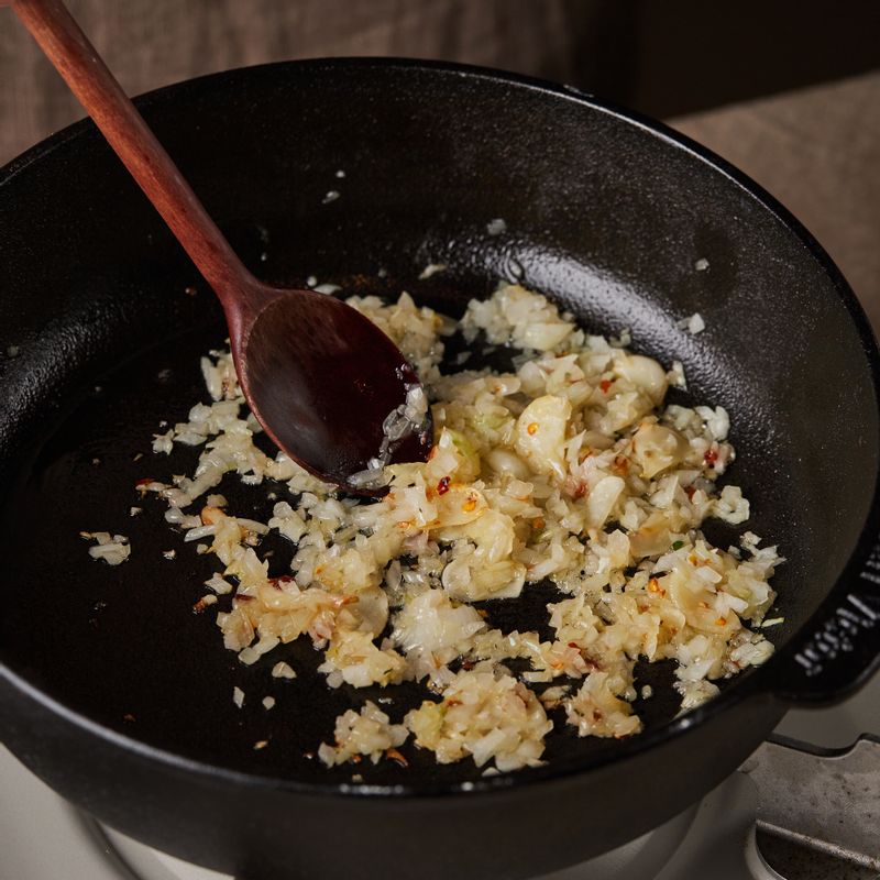 달군 팬에 올리브오일을 두르고 마늘과 페퍼론치노를 넣어 볶아주세요. 다진 양파를 넣고 갈색빛이 될 때까지 볶다가 소금 1작은술과 후추 약간을 넣어주세요. 토마토소스를 붓고 병에 물을 넣어 나머지 소스까지 모두 부은 후 7분간 중약불에서 끓여주세요.