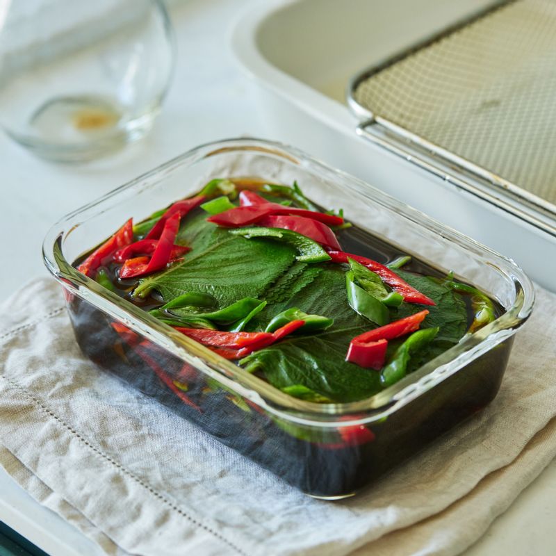밀폐 용기에 데친 깻잎과 고추를 담고 식힌 양념장을 부어주세요. 깻잎이 양념에 잠기도록 무거운 접시나 돌로 누른 후 뚜껑을 덮어 반나절 정도 숙성 시켜주세요.