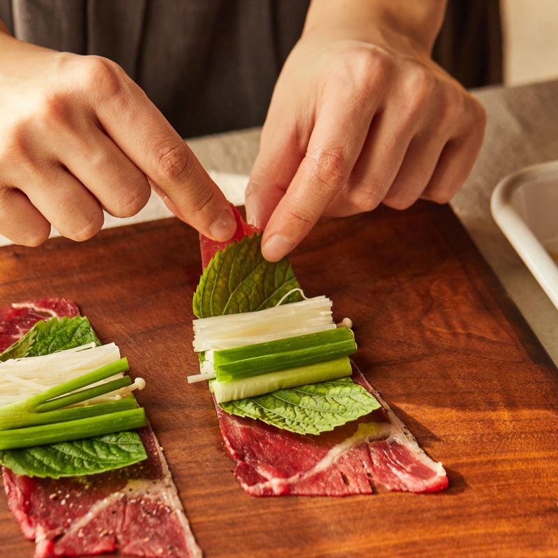밑간한 쇠고기에 깻잎을 깔고 팽이버섯과 쪽파를 올려 돌돌 말아주세요.