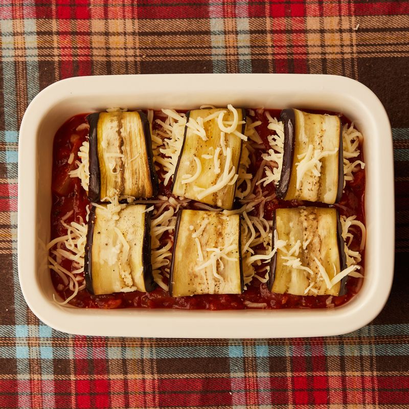 내열 용기에 토마토소스를 깔고 돌돌 말아둔 가지를 올린 후 모짜렐라와 파마산 치즈를 약간 뿌려주세요.