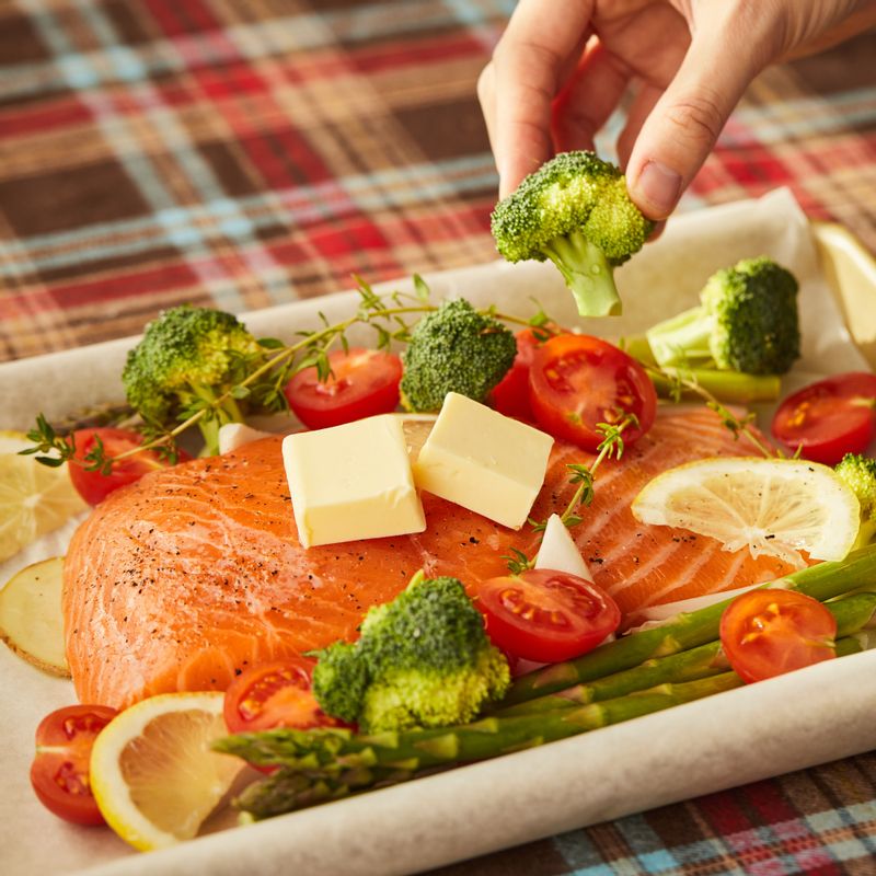 내열 용기에 종이호일을 깔고 감자와 양파, 아스파라거스, 브로콜리, 연어를 올려주세요. 연어 위에 레몬과 타임, 버터를 넣고 소금, 후춧가루를 뿌려주세요.