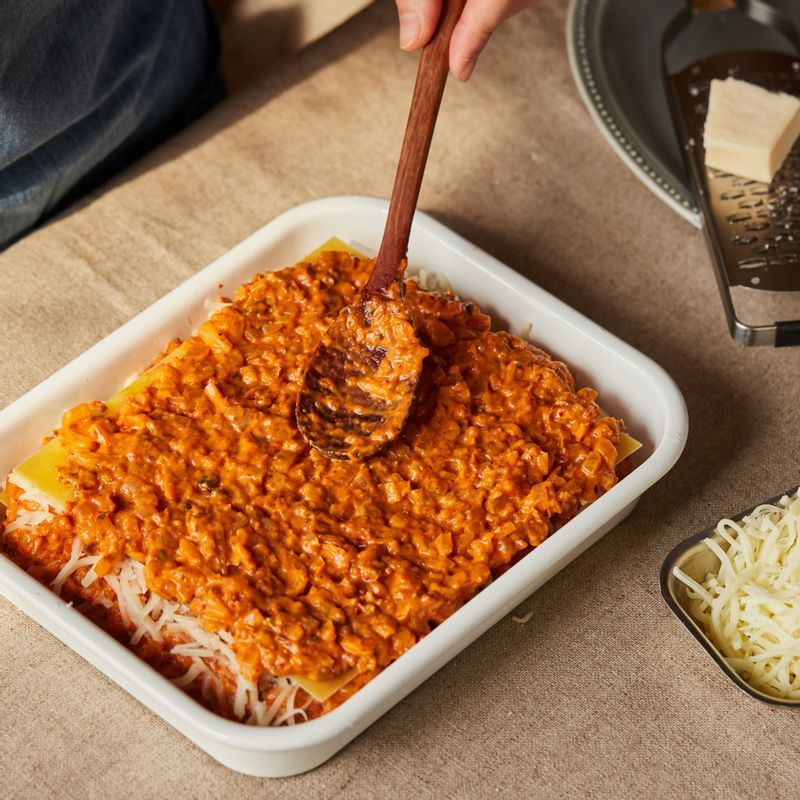 내열 용기에 소스를 얇게 깔고 라자냐 - 소스 - 모짜렐라 치즈, 파마산 치즈 순서로 반복해 쌓고 포일 또는 종이 포일로 덮어주세요.