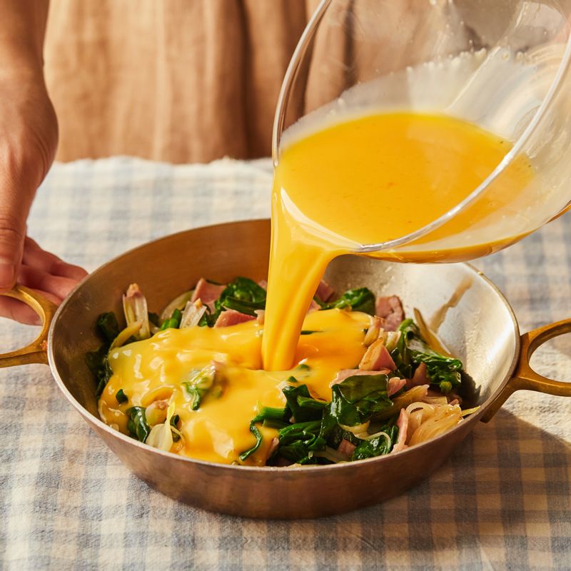 내열 용기에 볶은 재료와 달걀 물을 붓고 방울토마토를 얹은 후 슈레드 모짜렐라 치즈를 올려주세요.