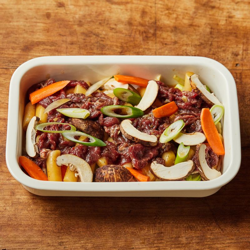 내열 용기에 떡과 소고기, 손질한 채소를 넣고 물을 부어 포일로 감싸주세요.