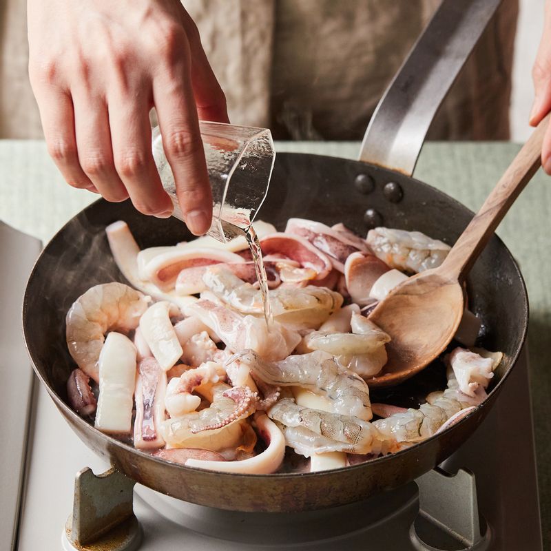 넓은 팬에 기름을 두르고 마늘 편을 넣어 볶다가 향이 올라오면 손질한 해물과 청주를 넣어서 센 불에서 2분 정도 볶아주세요.