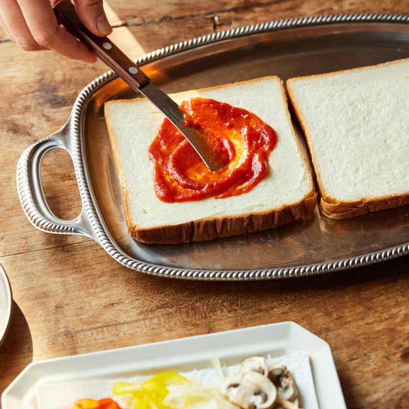 버터를 식빵 한 면에 바른 후 토마토소스를 발라주세요. 햄, 베이컨, 파프리카, 양파, 양송이 순으로 토핑해주세요.