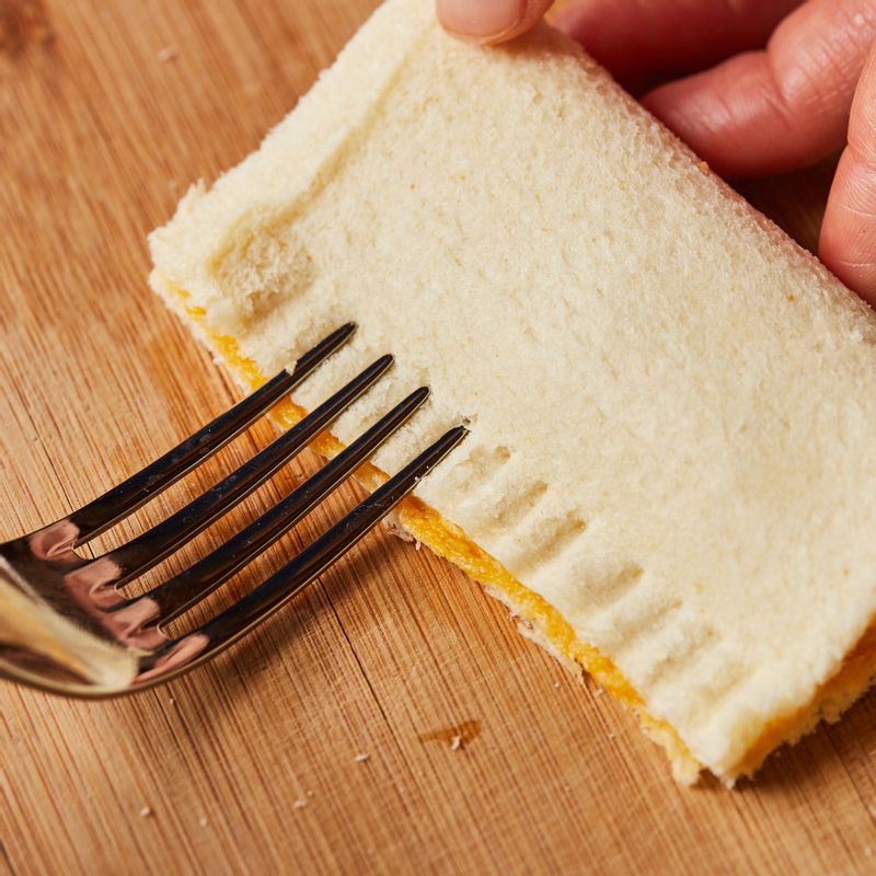 식빵 테두리 쪽에 달걀물을 발라 접어주고 포크로 테두리를 눌러 양쪽 면을 붙인 후 사과파이 중앙에 칼집을 넣고 윗면에 달걀물을 발라주세요.