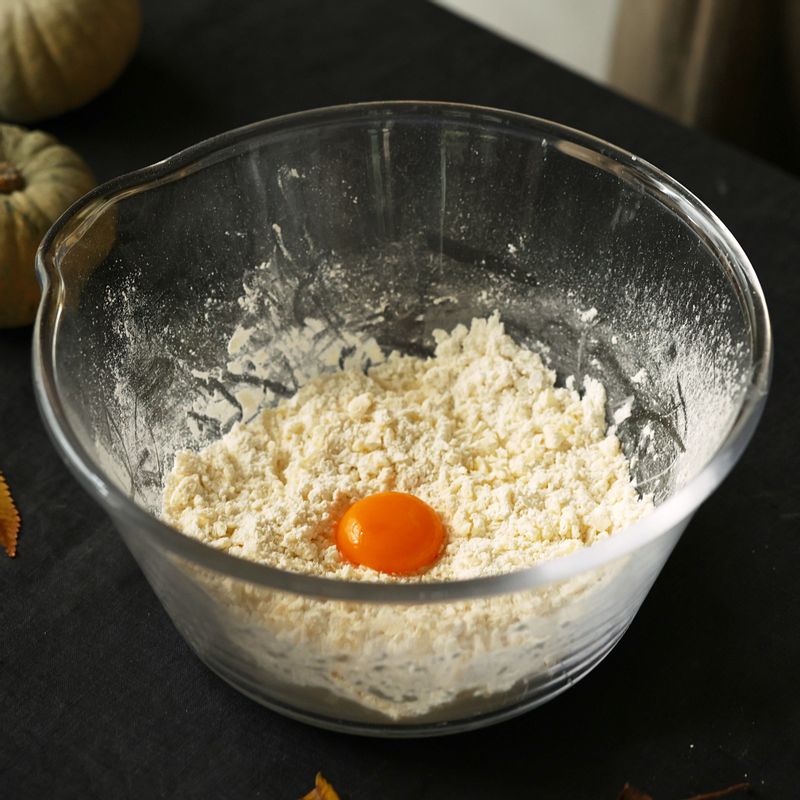 반죽이 부슬부슬한 상태가 되면 찬물과 달걀노른자를 넣고 스크래퍼로 자르듯이 돌려가며 섞어주세요.