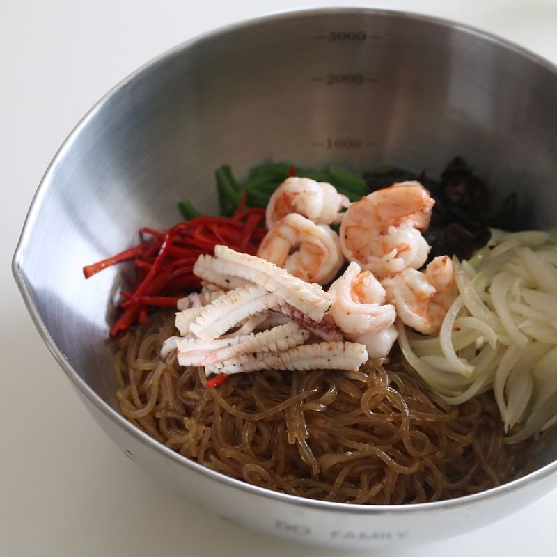 볼에 한 김 식힌 당면과 볶은 채소, 버섯, 오징어, 새우를 넣고 참기름을 약간 뿌려 버무려주세요.