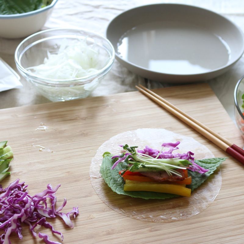 볼에 따뜻한 물을 준비하고 라이스페이퍼를 5초 정도 담갔다 꺼내 평평한 곳에 펼칩니다. 깻잎을 깔고 훈제오리와 채소를 골고루 올려주세요.