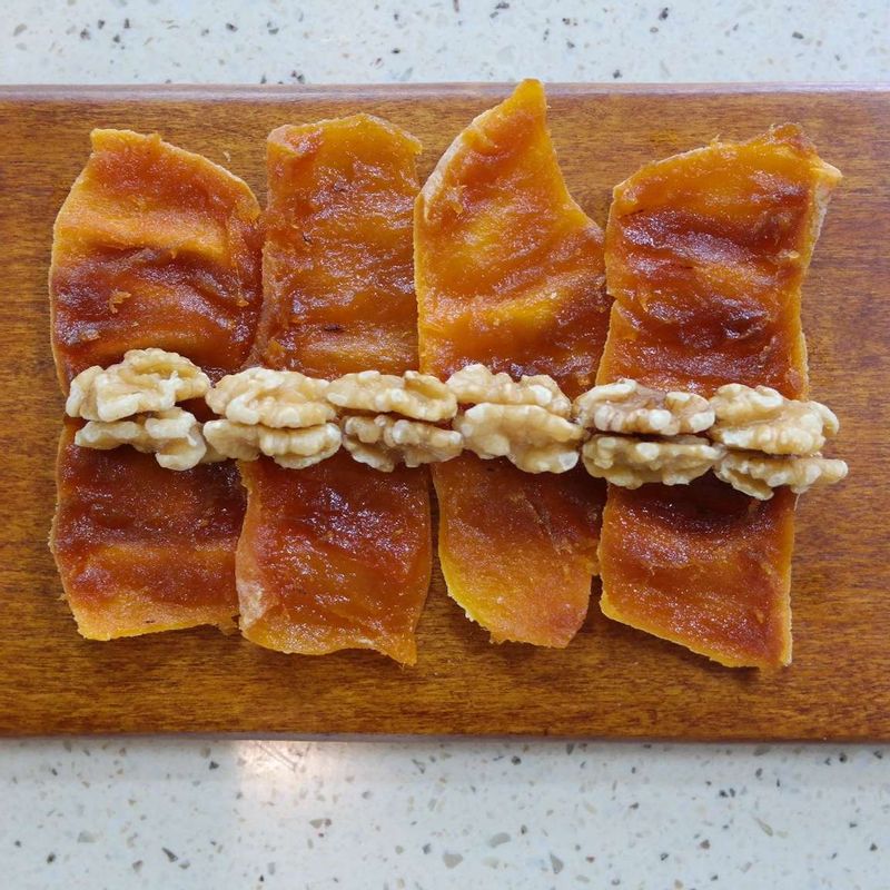 곶감 4~5개를 조금씩 겹치게 놓아주세요. 1/3 지점에 호두를 올리고 촘촘히 말아 랩을 씌워 냉동실에서 굳혀주세요. 김발로 말면 모양이 더 예뻐요.