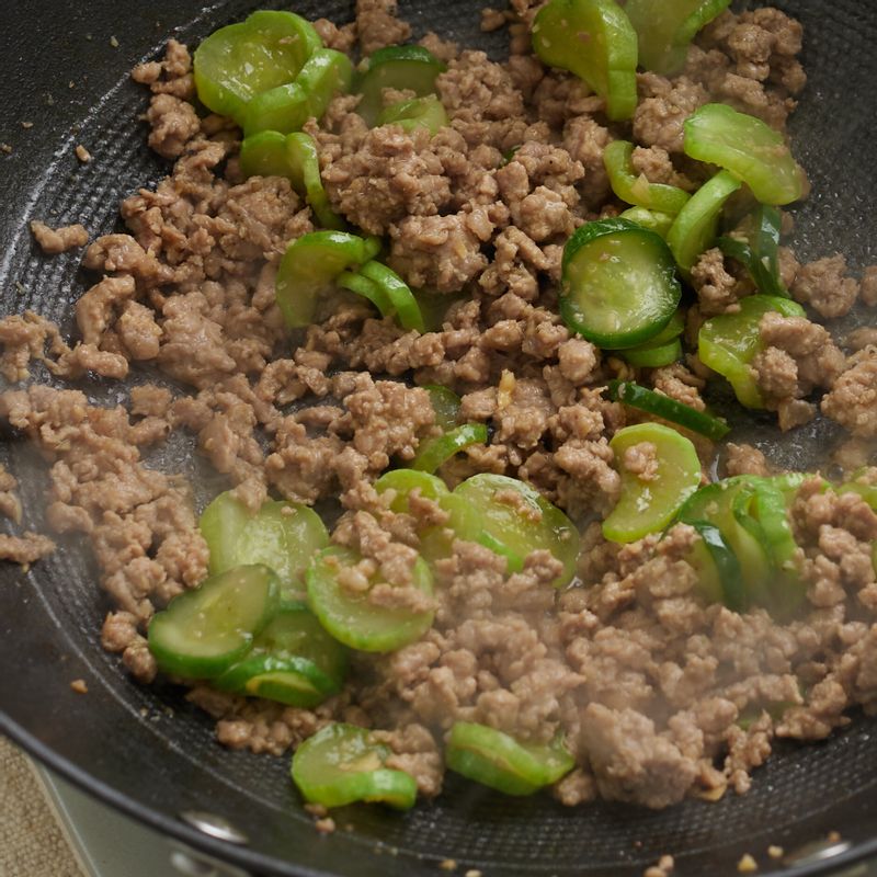 달군 팬에 식용유를 두른 후 돼지고기를 올려 중불에서 볶아주세요. 돼지고기가 어느 정도 익으면 오이를 넣어 센 불에서 빠르게 볶아주세요. 마지막으로 참기름과 통깨를 뿌려 마무리해 주세요.