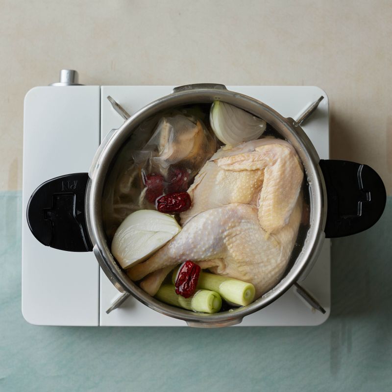 손질한 닭을 압력솥에 넣어주세요. 대파와 생강, 마늘, 양파, 삼계탕 재료를 국물팩에 담은 후 함께 넣어주세요.