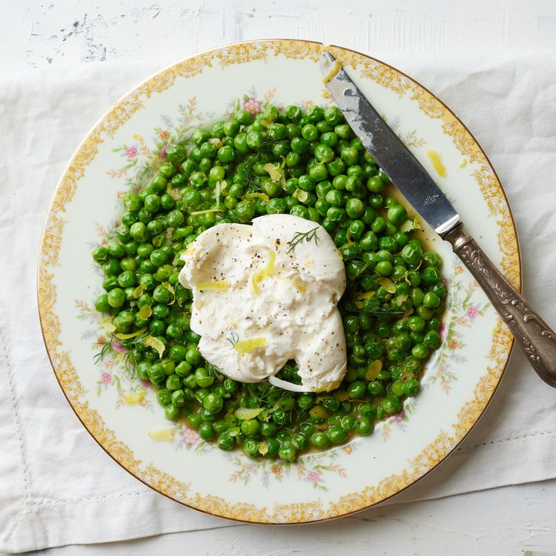 완두콩을 접시에 담고 부라타 치즈를 올려주세요. 딜과 레몬제스트, 후춧가루를 뿌려 완성해주세요.