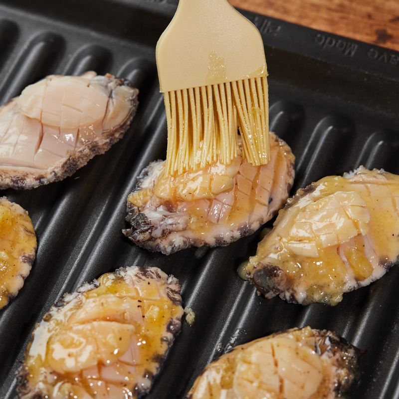 구이 전용 팬에 전복을 올린 후 녹인 버터와 다진 마늘, 후춧가루를 섞어 발라주세요.