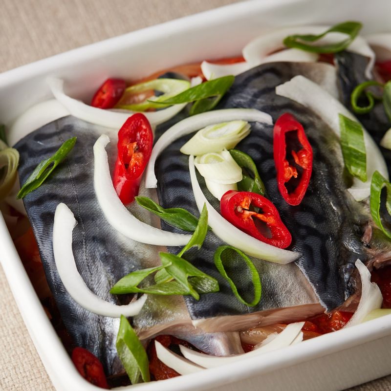 내열 용기에 묵은지를 깔고 고등어를 올린 후 손질한 채소와 양념을 넣어주세요.