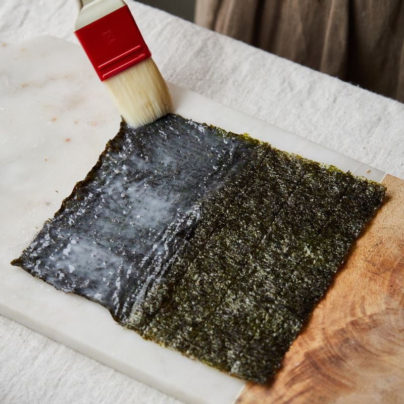 김의 거칠거칠한 부분 한쪽 면에 식힌 찹쌀풀을 얇게 펴 바르고 반으로 접은 후  4조각으로 길게 잘라주세요. 한 번 더 찹쌀풀을 발라준 후 통깨를 얹어주세요. 
(tip 찹쌀풀을 김의 가운데에서 바깥쪽으로 펴 가며 발라주면 김의 수축 현상을 줄 일 수 있어요)