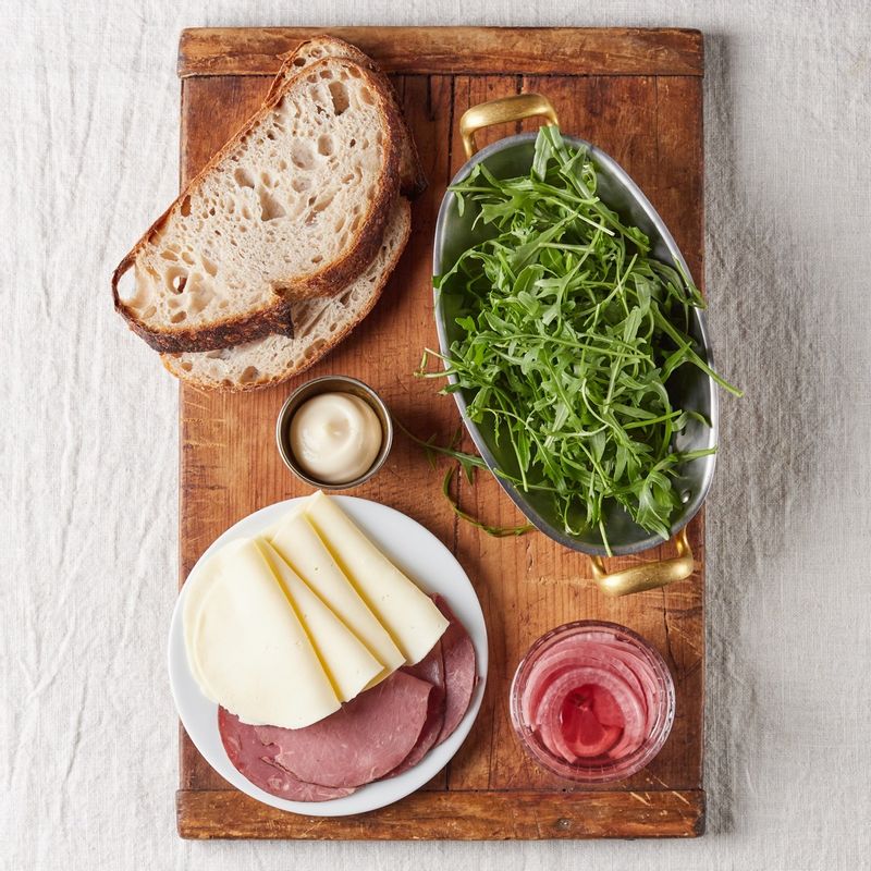 루꼴라 오픈 토스트을 위한 재료 이미지로 루꼴라,호밀빵,햄,슬라이스 치즈,양파 피클 등으로 구성 되어있습니다.