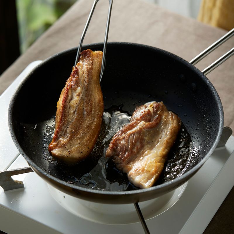 달군 팬에 오일을 두르고 통삼겹살을 올려주세요. 소금과 후춧가루를 뿌린 후 겉면을 바삭하게 구워주세요.