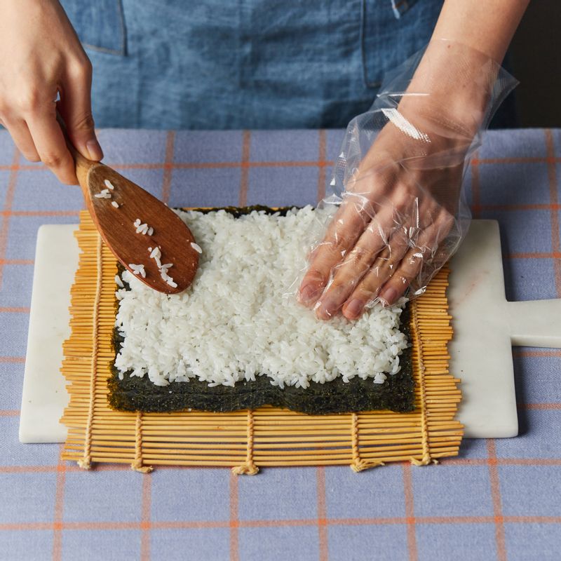 김밥용 김에 밥을 얇게 깔고 김으로 말아 둔 소시지를 가운데 넣고 돌돌 말아주세요.