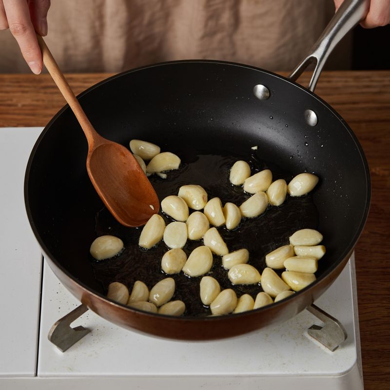 달군 팬에 기름을 두른 후 깐 마늘을 넣어 약한 불에서 노릇노릇하게 볶아주세요.