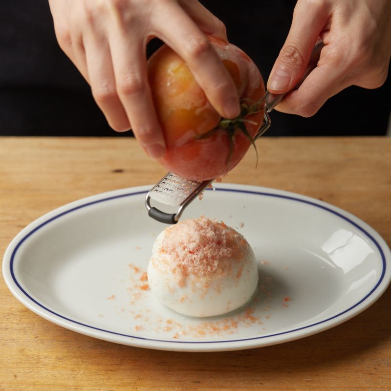 접시에 부라타 치즈를 넣은 후 얼린 토마토를 치즈 그레이터로 갈아주세요.