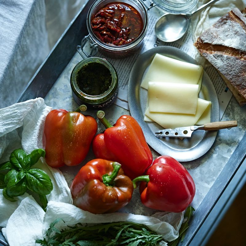 그릴드 벨 페퍼 샌드위치을 위한 재료 이미지로 샌드위치용 빵,슬라이스 치즈,빨간 파프리카,루꼴라,바질 페스토 등으로 구성 되어있습니다.