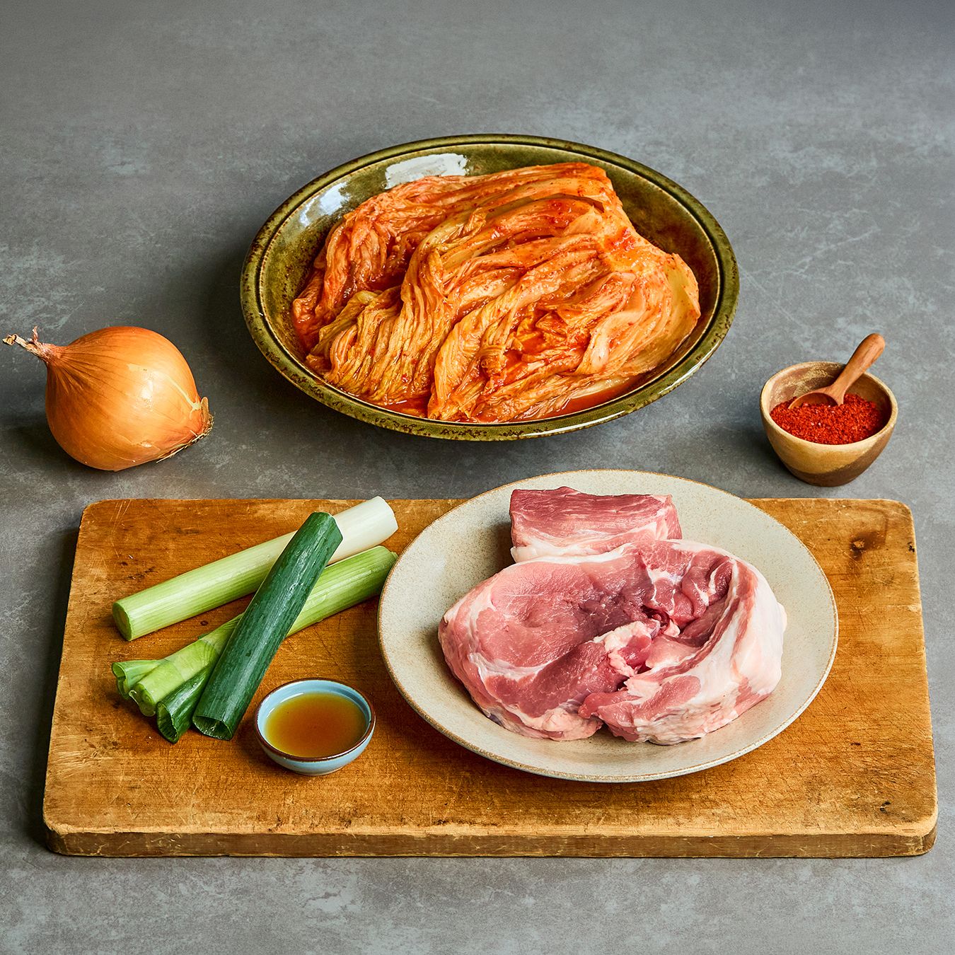 밥솥 돼지고기 김치찜을 위한 재료 이미지로 돼지고기 목살(또는 앞다리살),김치,김치국물,양파,대파 등으로 구성 되어있습니다.